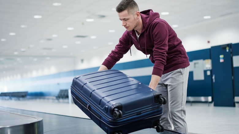 man picking up blue luggage