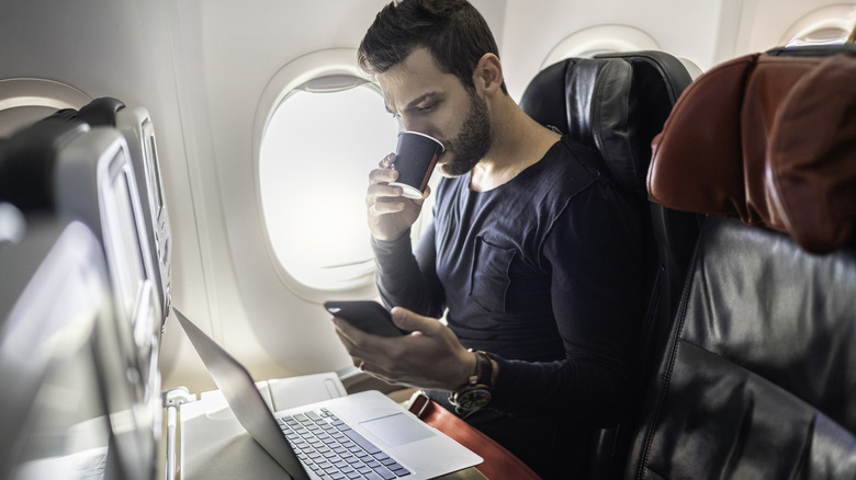 man using phone and laptop on plane